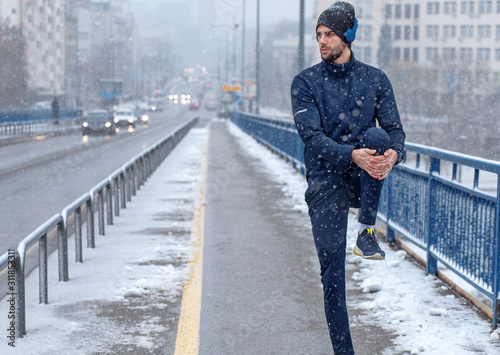 Young man stretching before running in city street at cold winter day. © Zoran Zeremski
