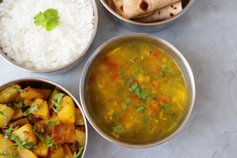 Stainless steel Lunch Box or Tiffin with Indian food menu Chapati or Roti, Garlic Dal Tadka, White Rice and Potato or Jeera aloo. with spoons, tissue paper and glass of water. Copy space