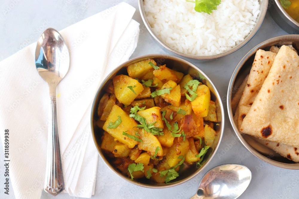 Stainless steel Lunch Box or Tiffin with Indian food menu Chapati or Roti, Garlic Dal Tadka, White Rice and Potato or Jeera aloo. with spoons, tissue paper and glass of water. Copy space Stainless steel Lunch Box or Tiffin with Indian food menu Chapati or Roti, Garlic Dal Tadka, White Rice and Potato or Jeera aloo. with spoons, tissue paper and glass of water. Copy space