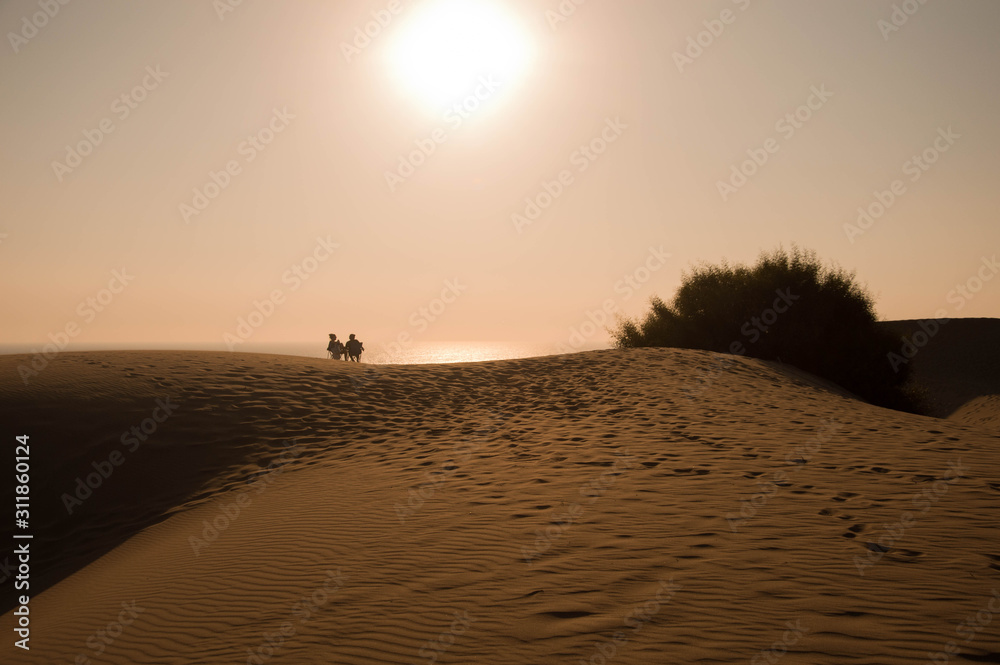 Two person sitting on the sand hill against the sun at Patara, Antalya