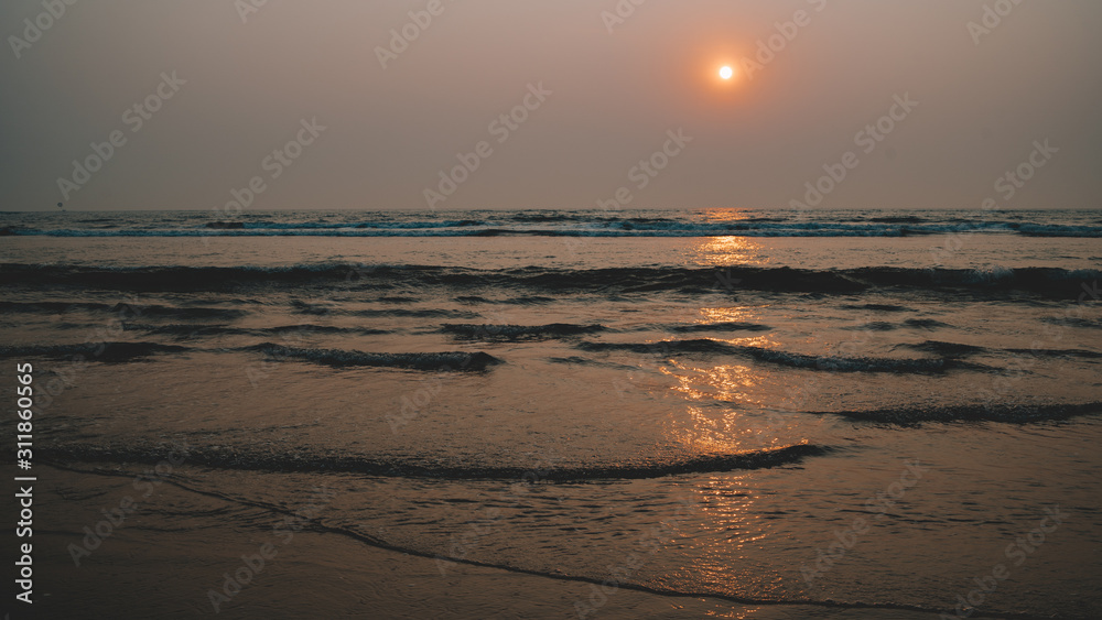 Sunset over sea and beach. Cloudless sundown sky over waving sea and sandy beach in evening on resort