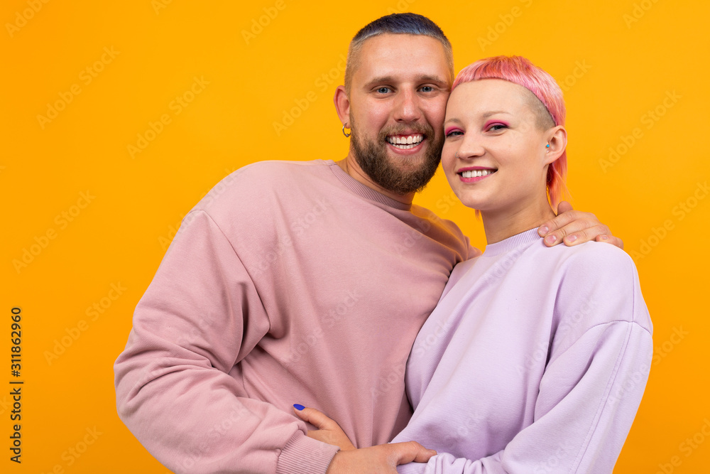 Obraz premium Unusual pretty woman with short pink hair and tattoo hugs with her boyfriend isolated on orange background