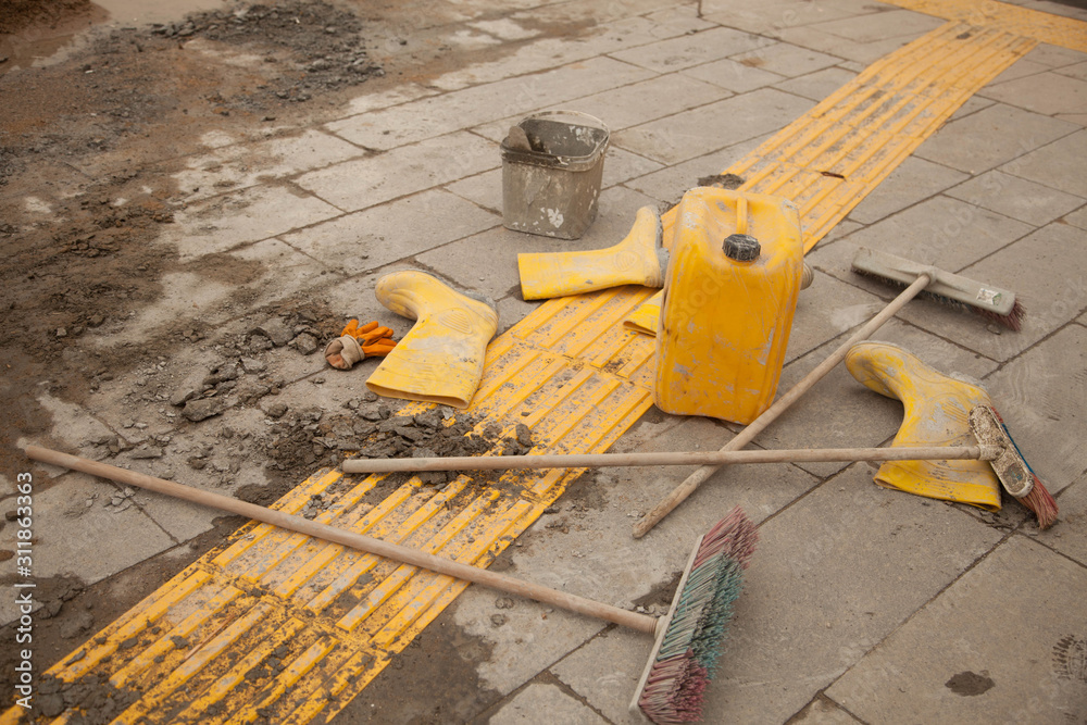 Yellow boots, yellow jerry can and broom on construction site with flower