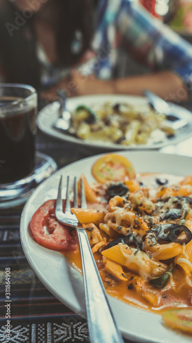 Delicious pasta with tomato sauce. Silverware placed on plate of palatable pasta with tomato sauce and olives on ornamental table in cafeteria