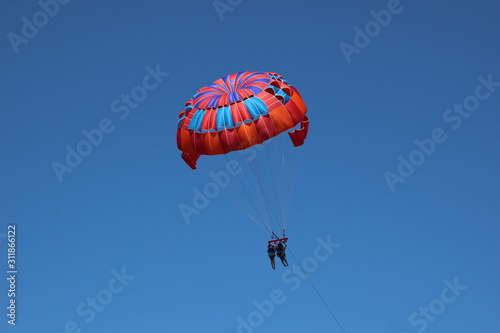 parasailing in summer with colorful parachute, two persons in blue sky
