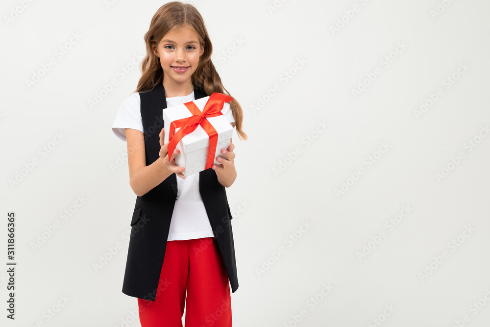 Fototapeta premium Teenager caucasian girl in black jacket, white shirt and red pants holds a white box with gift and rejoices isolated on white background