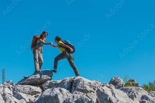 A woman helps her friend climb a stone.