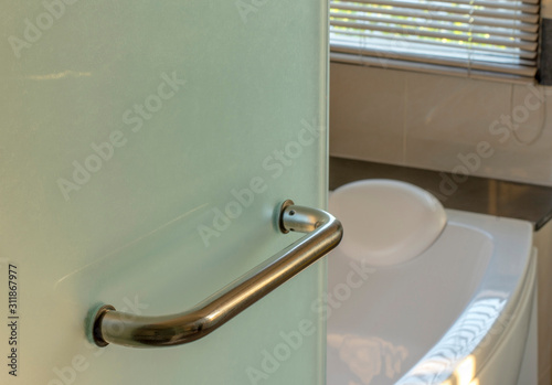  Modern bathroom glass door handle detail with bath tub in the background.