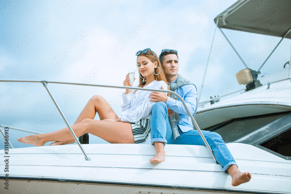 Lovers spending happy time on a yacht at sea. Luxury honeymood on a seaboat. Vacation, travel, sea, friendship and people concept. Smiling couple sitting and talking on yacht deck