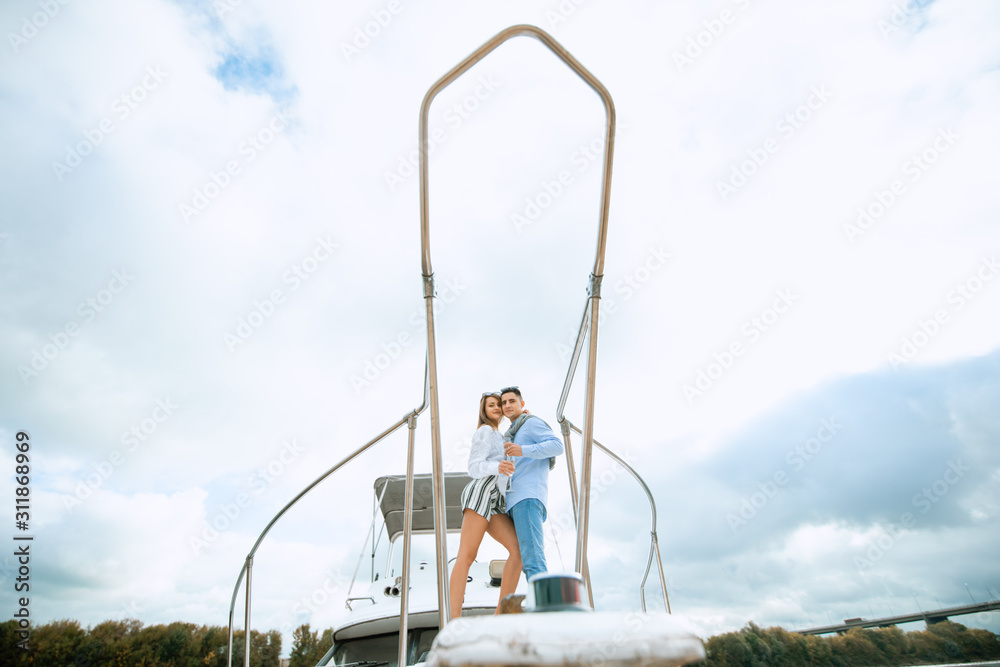 Naklejka premium Romantic couple in love on sail boat at under sunlight on yacht. Happy exclusive alternative lifestyle concept. Love story of two lovers. Two young tourists having fun on boat tour in the summertime
