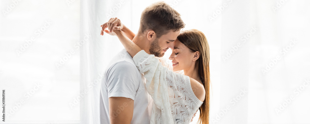 panoramic shot of attractive and smiling woman hugging handsome man in apartment panoramic shot of attractive and smiling woman hugging handsome man in apartment