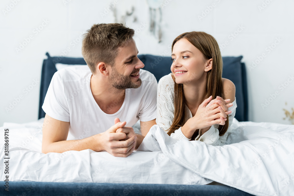attractive and smiling woman looking at handsome man in apartment attractive and smiling woman looking at handsome man in apartment
