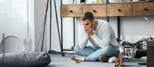panoramic shot of handsome and shocked man obscuring face in robbed apartment