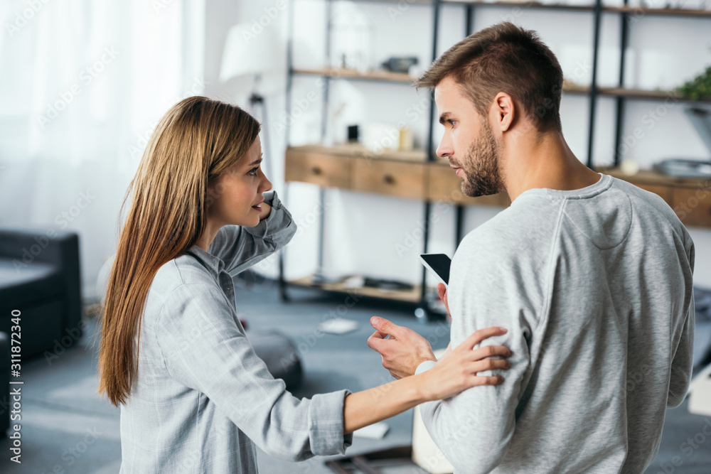 sad woman talking with handsome man with smartphone in robbed apartment sad woman talking with handsome man with smartphone in robbed apartment