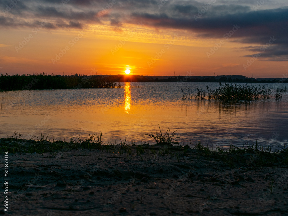 landscape with sunset in the background, lake sand and grass in the foreground