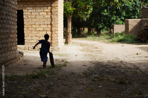 Back View Of An Unidentified Little African Village Girl Playing With An Old Wheel