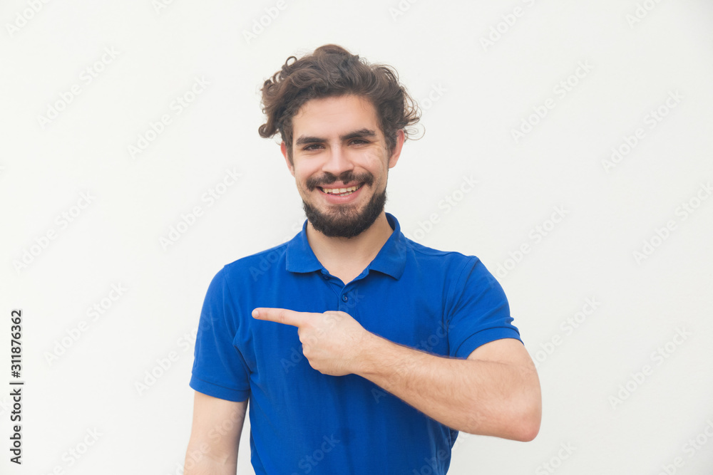 Cheerful positive customer pointing finger away at copy space. Handsome bearded young man in blue casual t-shirt posing isolated over white background. Advertising concept Cheerful positive customer pointing finger away at copy space. Handsome bearded young man in blue casual t-shirt posing isolated over white background. Advertising concept