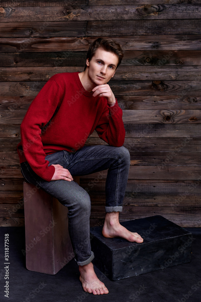 Portrait of a handsome young man. Short-haired Caucasian in a burgundy sweater on a vintage wood background. Cute looks at the camera, sitting on a stand. Loft style concept. Portrait of a handsome young man. Short-haired Caucasian in a burgundy sweater on a vintage wood background. Cute looks at the camera, sitting on a stand. Loft style concept.