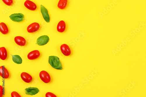 Red tomatoes and basil leaves on yellow background. Top view and copy space.