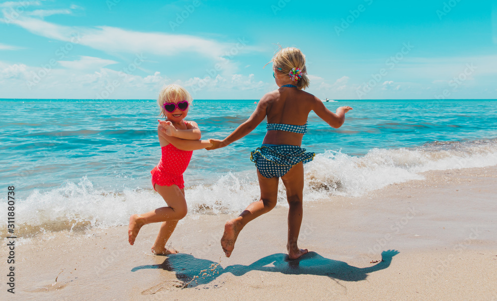 happy little girls play with waves on beach, kids enjoy vacation