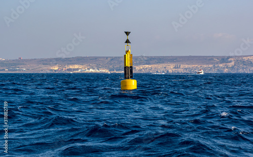 Yellow and black steel navigational floating buoy - West cardinal mark - in the blue Mediterranean sea water between Comino and Malta islands.