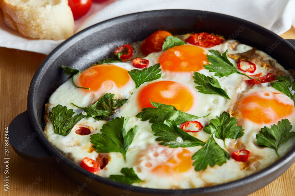 close up view of fried eggs with parsley and chili pepper in pan on wooden table close up view of fried eggs with parsley and chili pepper in pan on wooden table