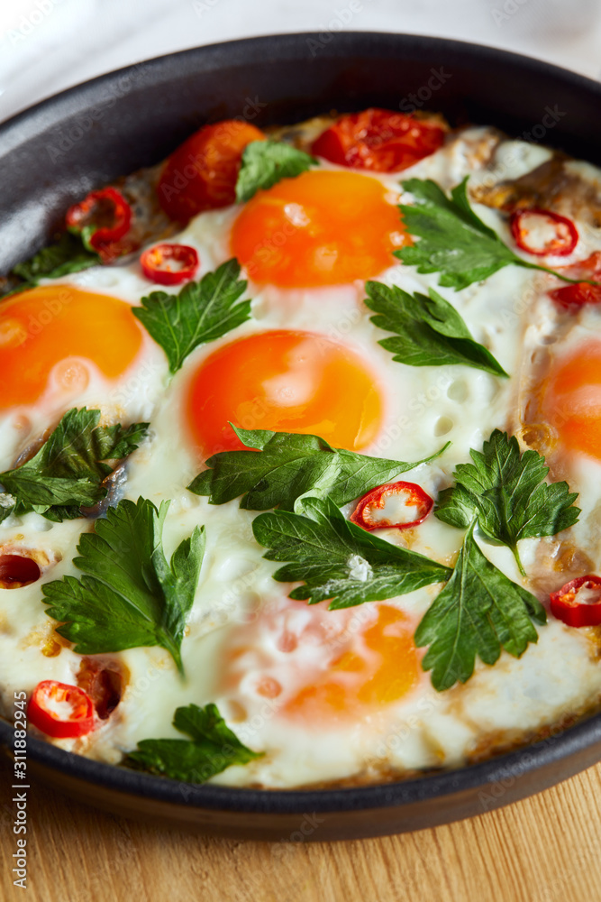close up view of fried eggs with parsley and chili pepper in pan on wooden table close up view of fried eggs with parsley and chili pepper in pan on wooden table