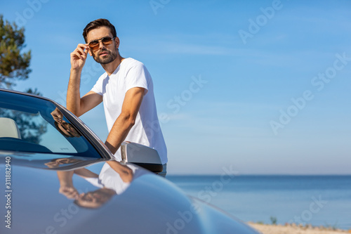 man touching sunglasses and standing near the cabriolet