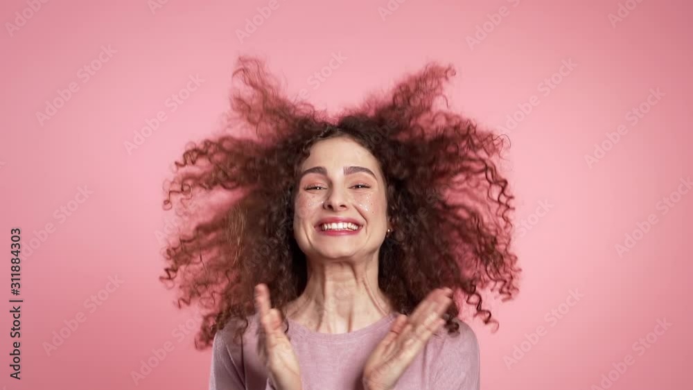 Excited girl with curly hair and unusual glitter makeup applauding, jumping, having fun, rejoices over pink studio background. Concept of happiness, winning, excellent news. Slow motion. Excited girl with curly hair and unusual glitter makeup applauding, jumping, having fun, rejoices over pink studio background. Concept of happiness, winning, excellent news. Slow motion.