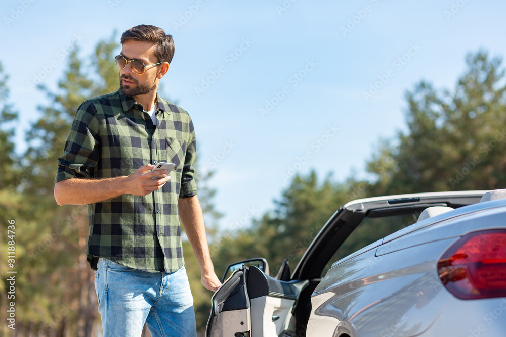 guy holding smartphone in the hand and opening door of his convertible