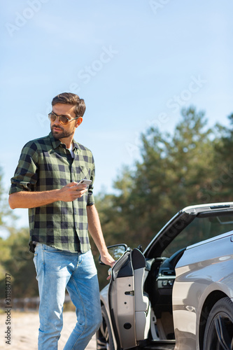 man opening door of the car and holding smartphone in the hand