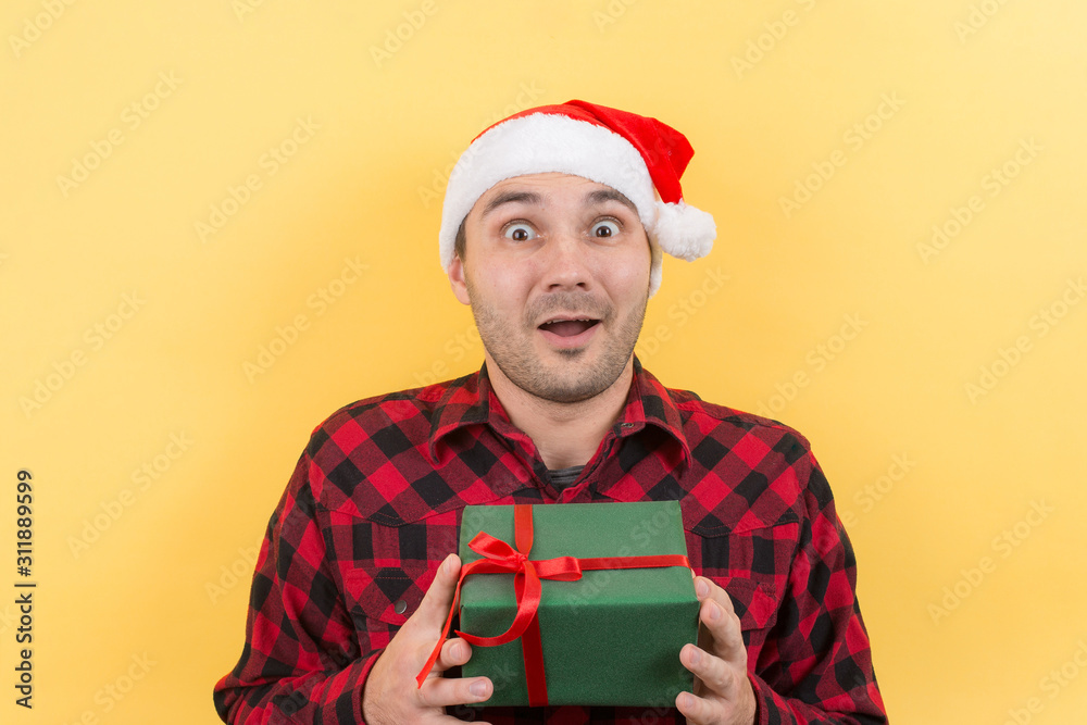 Happy surprised man in a red hat holding a gift with admiration on his face. Positive human emotions at christmas. Yellow background, copy space. Happy surprised man in a red hat holding a gift with admiration on his face. Positive human emotions at christmas. Yellow background, copy space.