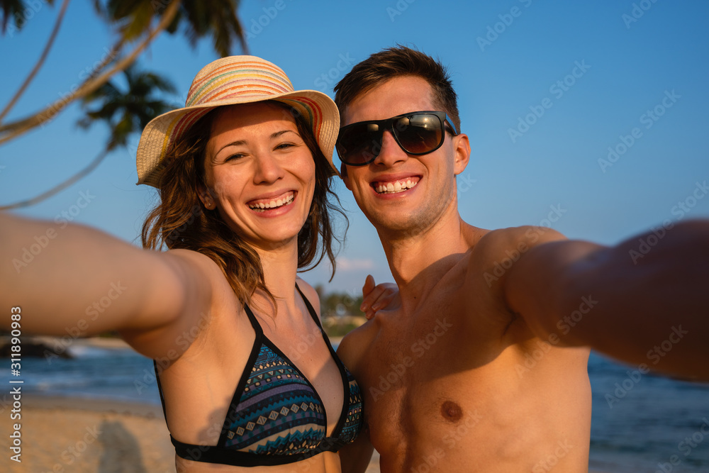 young happy couple taking a selfie in a tropical beach during sunset