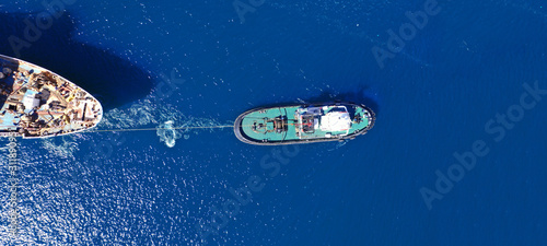Aerial drone ultra wide photo of industrial tug assisting boat ass in deep blue Mediterranean sea