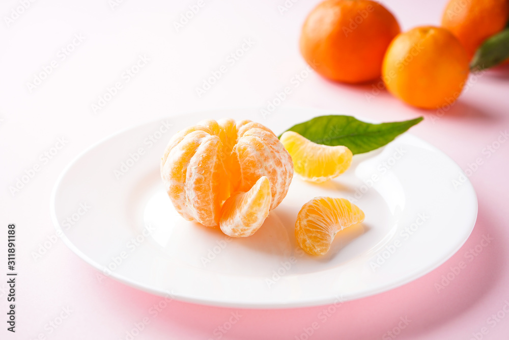 Tangerines with a green branch and slices in a white plate on a pink background. Tangerines with a green branch and slices in a white plate on a pink background.