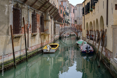 Narrow canal between residential buildings, old walls, boats on the water. Venice, Italy.
