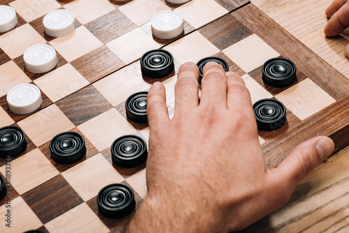 Cropped view of man playing black checkers on chessboard on table