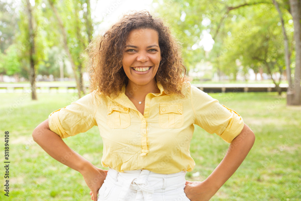Outdoor portrait of positive joyful woman in summer park with green grass in background. Curly haired black woman in casual posing outdoors. Happy woman outside concept Outdoor portrait of positive joyful woman in summer park with green grass in background. Curly haired black woman in casual posing outdoors. Happy woman outside concept