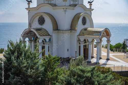 Malorechenskoye, Crimea, Russia - October 01, 2019. Church of St. Nicholas Mira patron saint of travelers and sailors on seashore. Observation deck around temple against blue surface of Black Sea. photo