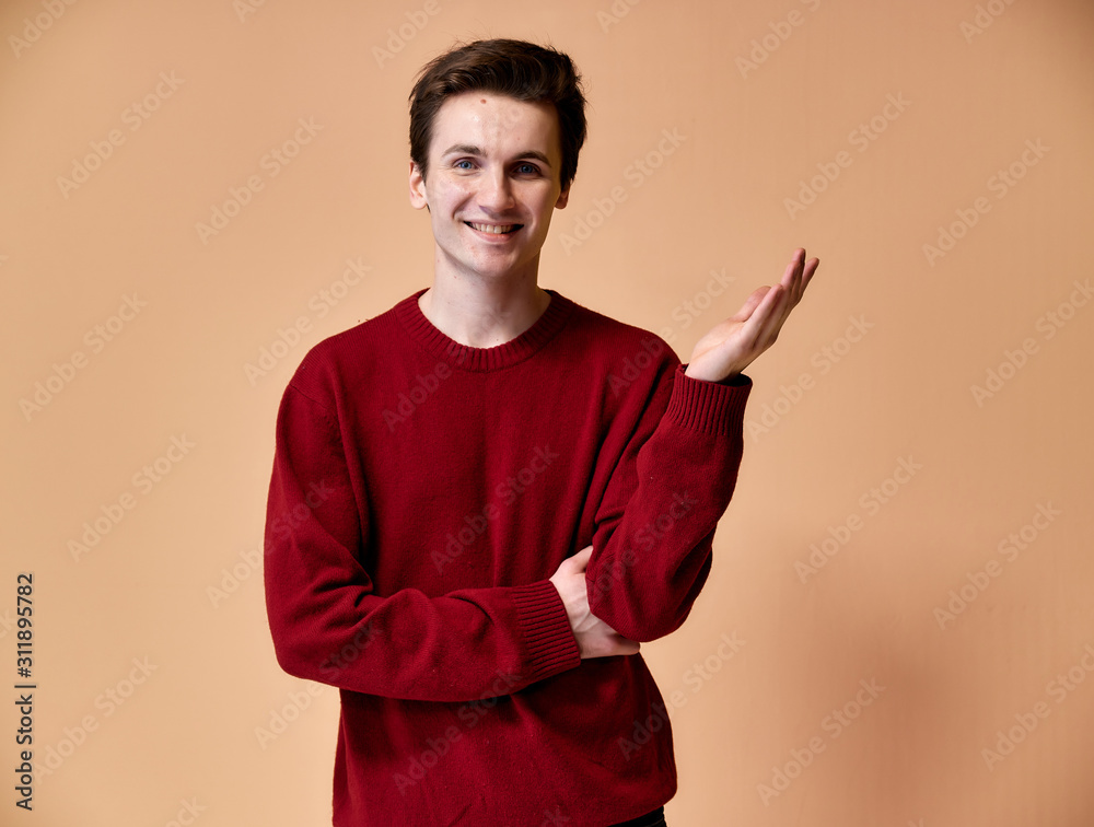 Portrait of a young Caucasian man with short hair and a white-toothed smile in a burgundy sweater on a pink background. Standing and talking right in front of the camera showing hands. Portrait of a young Caucasian man with short hair and a white-toothed smile in a burgundy sweater on a pink background. Standing and talking right in front of the camera showing hands.