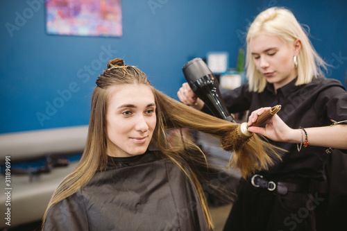 Portrait of happy woman at the hair salon. Professional hair styling concept. Hairdresser drying girl long hair using hairdryer and brush. Drying With Blow Dryer