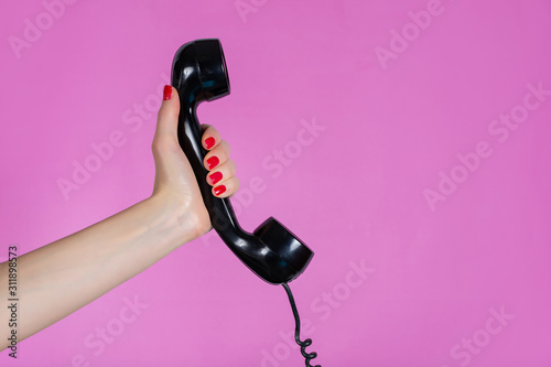 Female hand holding old and retro telephone headset isolated on pink background in studio. Girl hands with red manicure on fingers. Minimalism and retro concept
