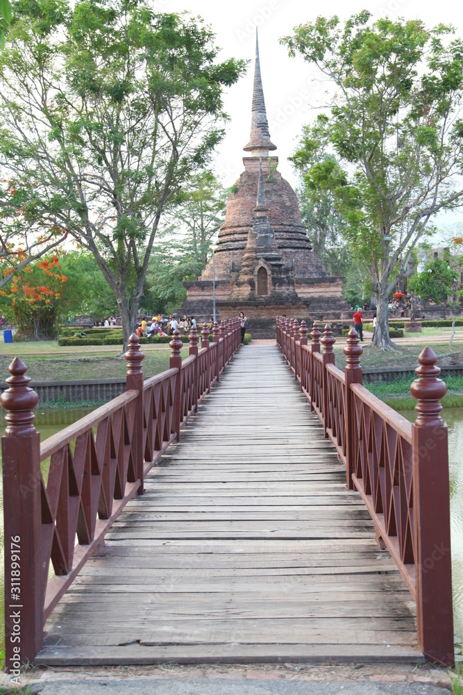 Wooden red bridge. Cross a pond to the temple in Sukhothai Historical Park, Thailand