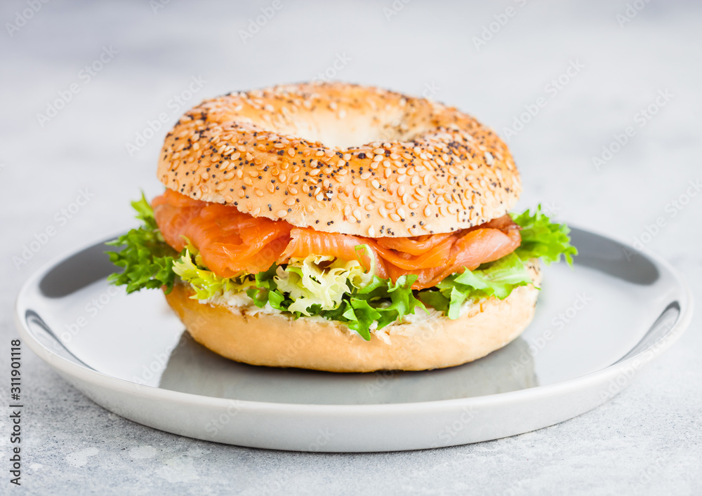 Fresh healthy bagel sandwich with salmon, ricotta and lettuce in grey plate on light kitchen table background. Healthy diet food.