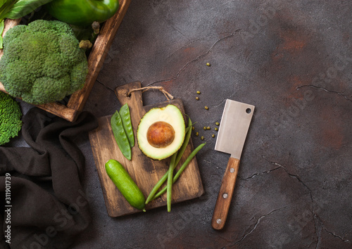 Assorted green toned raw organic vegetables in wooden box on dark background. Avocado, cabbage, cauliflower and cucumber with trimmed and mung beans and chopping board with knife. photo