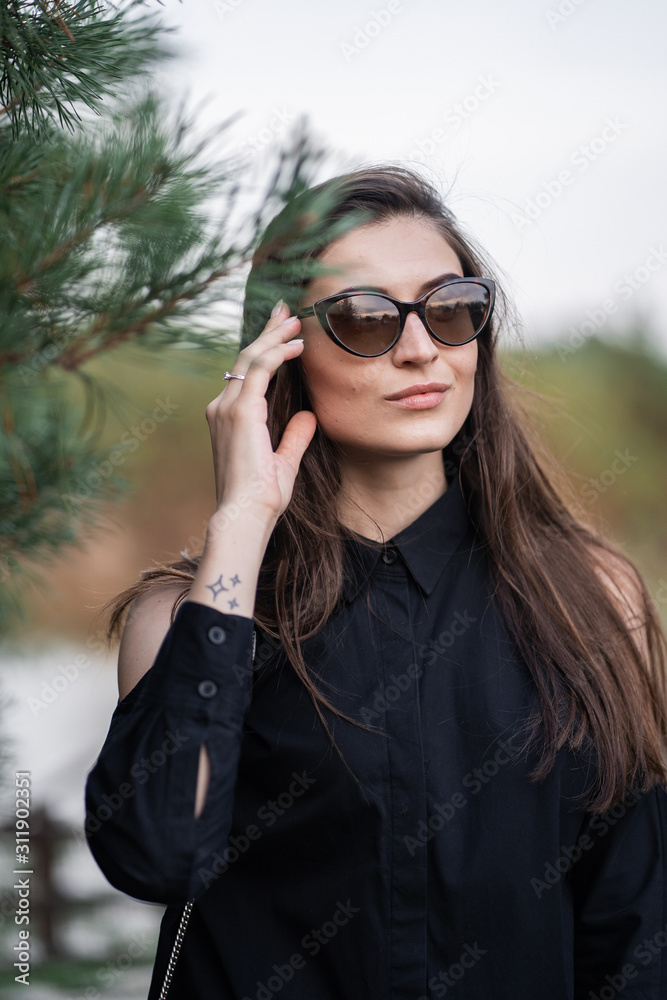 Beautiful woman with brunette hair in dark clothes and sunglasses. Fashion street photography. Fashion model is posing on nature background. sunglasses shop