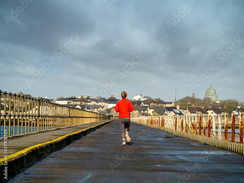 Woman running on asphalt road in red shirt, Town in the background. concept fitness, sport, physical activity.