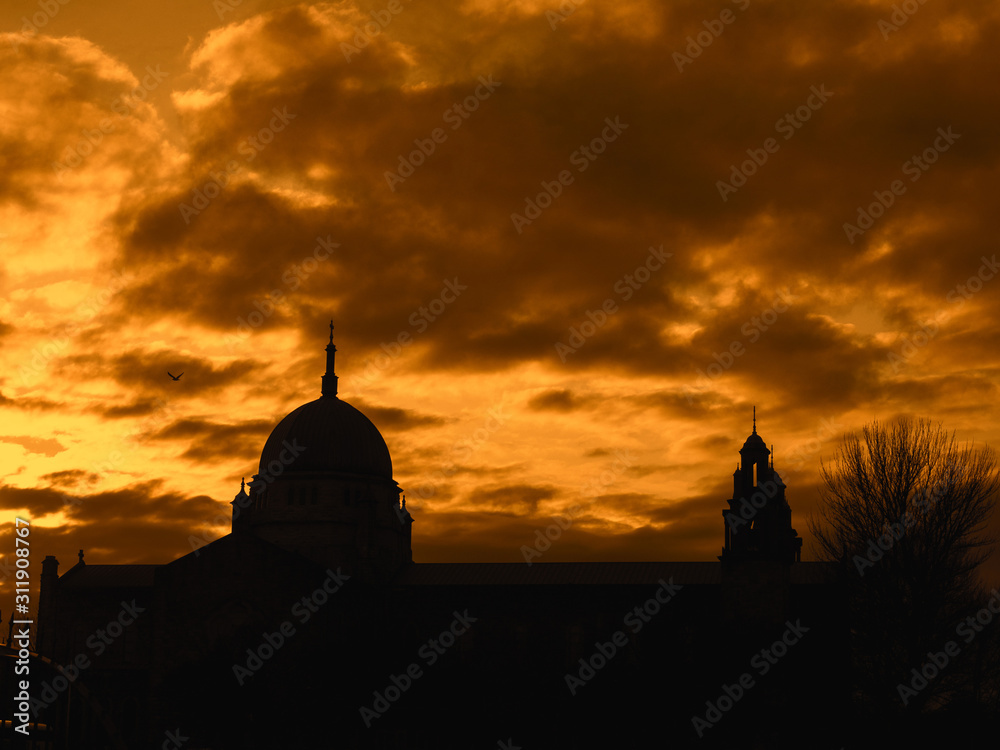 Silhouette of Galway Cathedral against warm orange sunset sky. Galway city, Ireland.