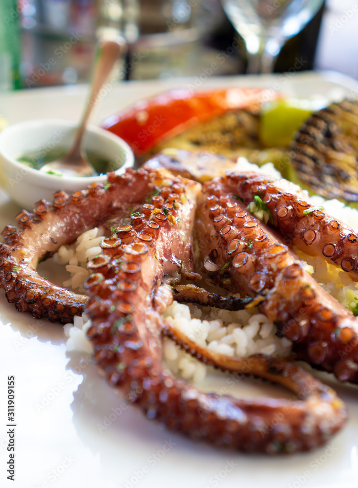 Grilled octopus on a bed of white rice and grilled vegetables. Garlic and parsley sauce. Typical healthy Montenegrin food Grilled octopus on a bed of white rice and grilled vegetables. Garlic and parsley sauce. Typical healthy Montenegrin food