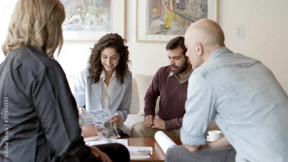 Interior designer talking with clients at home. Cheerful women and men sitting in living room at home and talking. Renovation discussion concept